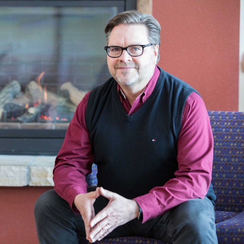 Larry Dutmer sits in front of a fireplace.